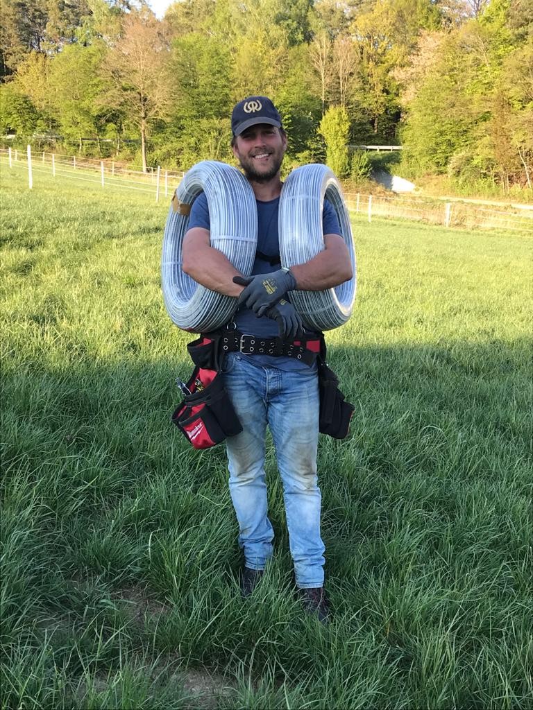 Daniel Schnyder auf der Ranch, mit Werkzeug und zwei Drahtrollen auf den Schultern